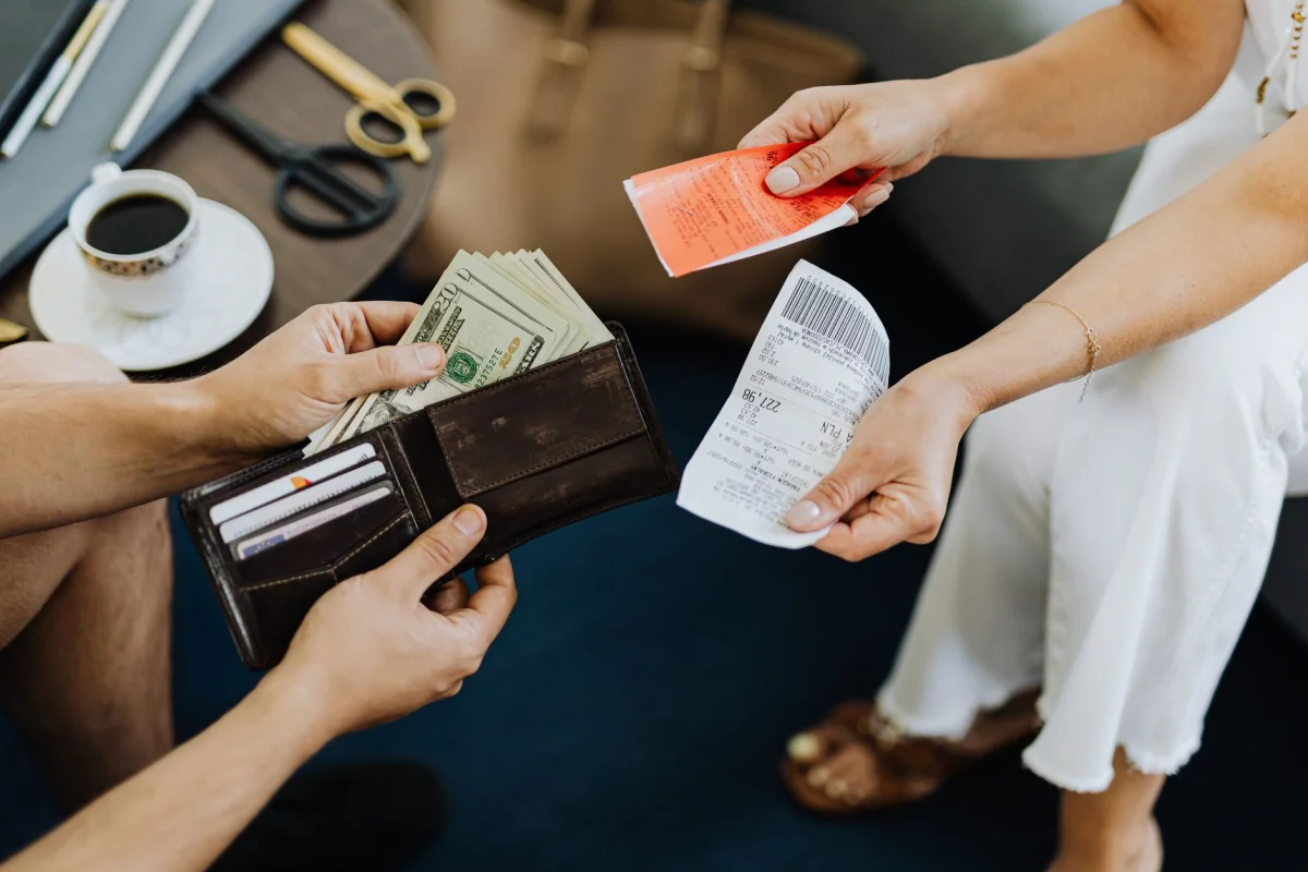 person counting cash bills pulled from a wallet on a table