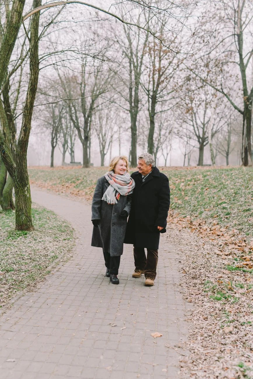 An older couple walking together along a tree lined park path
