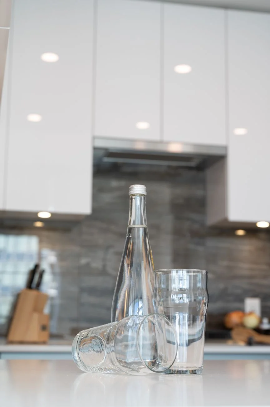 A glass water bottle filled with water sitting on a kitchen counter in natural light