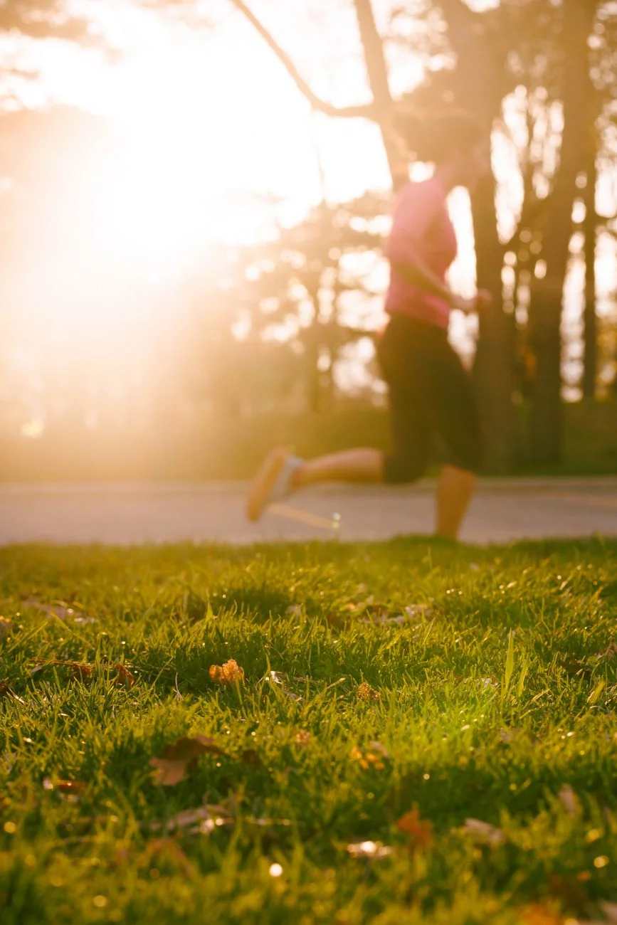 A runner jogging along a park path at sunrise