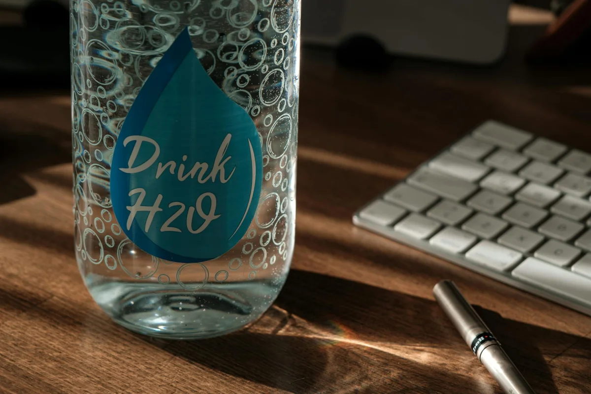 Glass of water and water bottle on a clean desk representing daily hydration habits