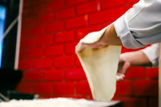 Hands stretching fresh pizza dough on a floured surface