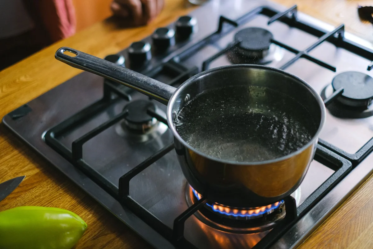 A pot of water boiling on a stovetop with rising steam